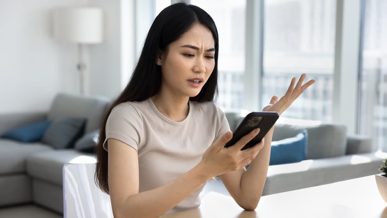 Young woman looks at smartphone screen with dissatisfied expression