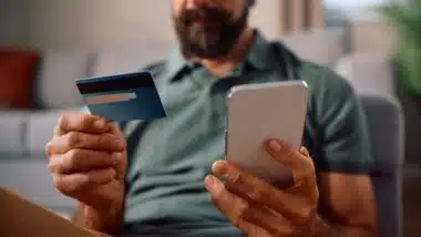Close up of man using credit card while paying over smart phone at home.
