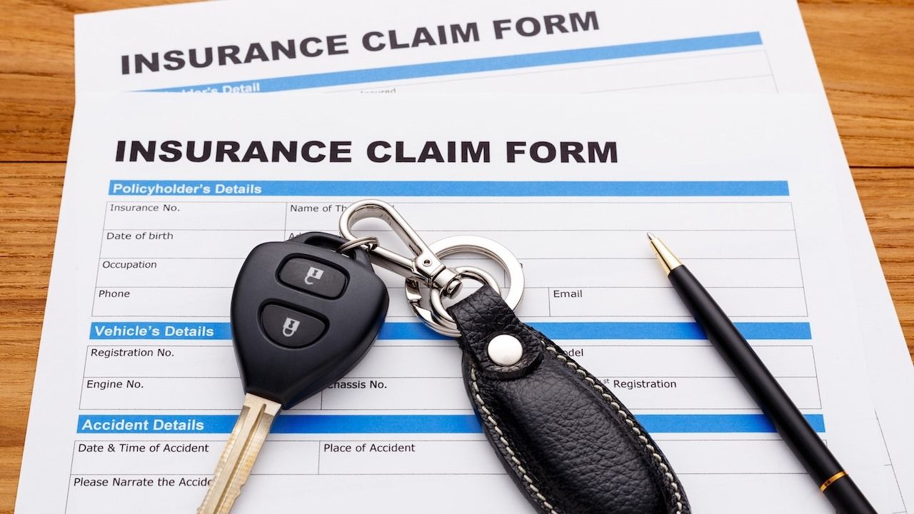 Insurance claim form with car key and pen on wood desk