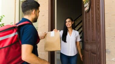 Happy Latin woman receiving a food order from a delivery man with a thermal backpack