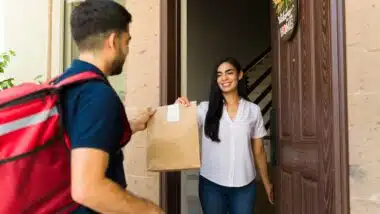 Happy Latin woman receiving a food order from a delivery man with a thermal backpack