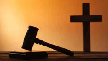 Silhouette of judge's gavel and cross on wooden table