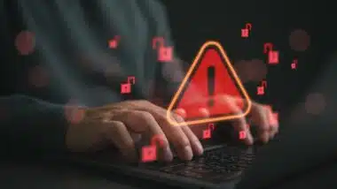 Hands typing on laptop with cybersecurity warning alert and unlocked padlock icons. Data breach risk, hacking attack, ransomware threat, online security vulnerability concept for business protection.