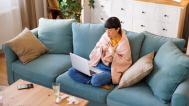 woman sitting on living room couch covered with blanket scheduling appointment through portal