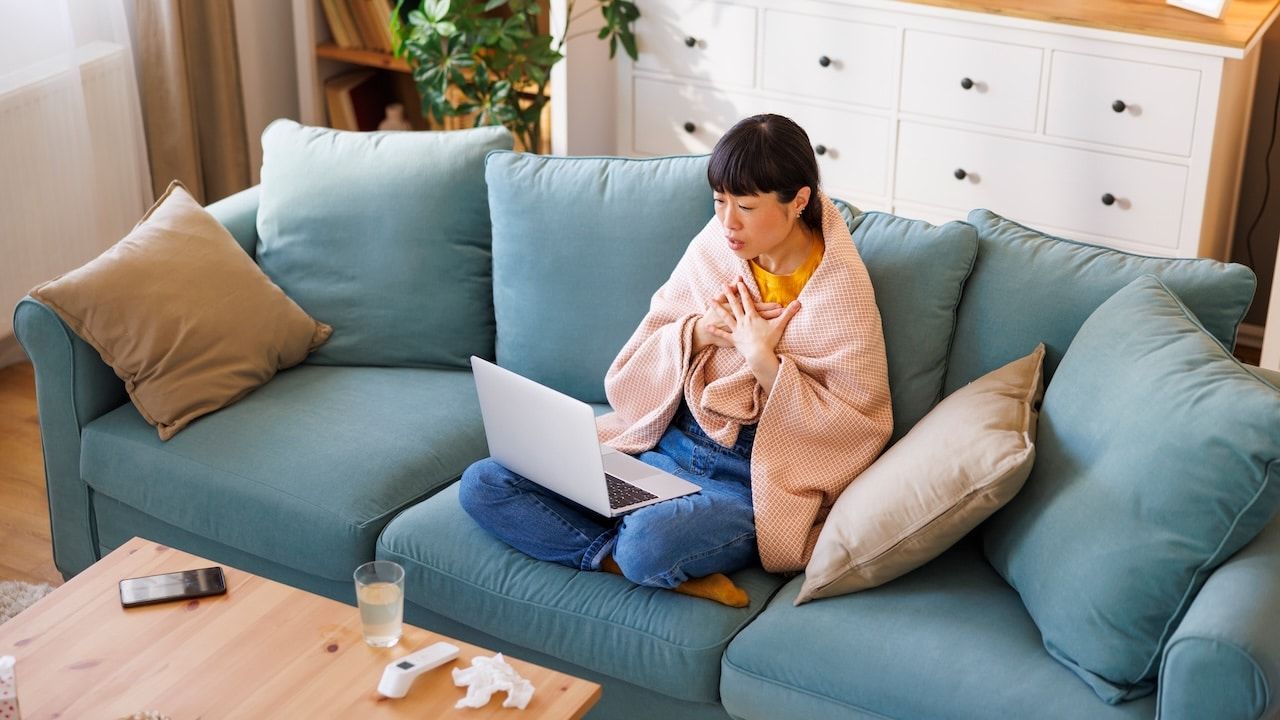 woman sitting on living room couch covered with blanket scheduling appointment through portal