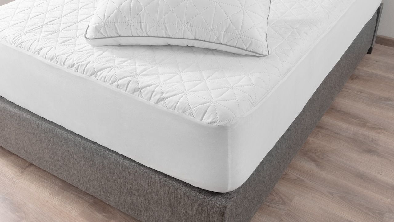 Close-up View of Pristine White Bed, Geometric Quilting on Mattress and Pillow, Contrasting with Soft Gray Upholstered Bed Frame, Comfort, Set Against a Warm Wooden Floor Background.