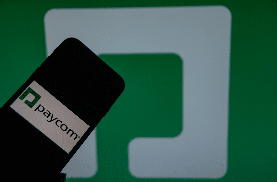 Paycom logo on phone in front of bigger Paycom logo, representing the Paycom settlement.