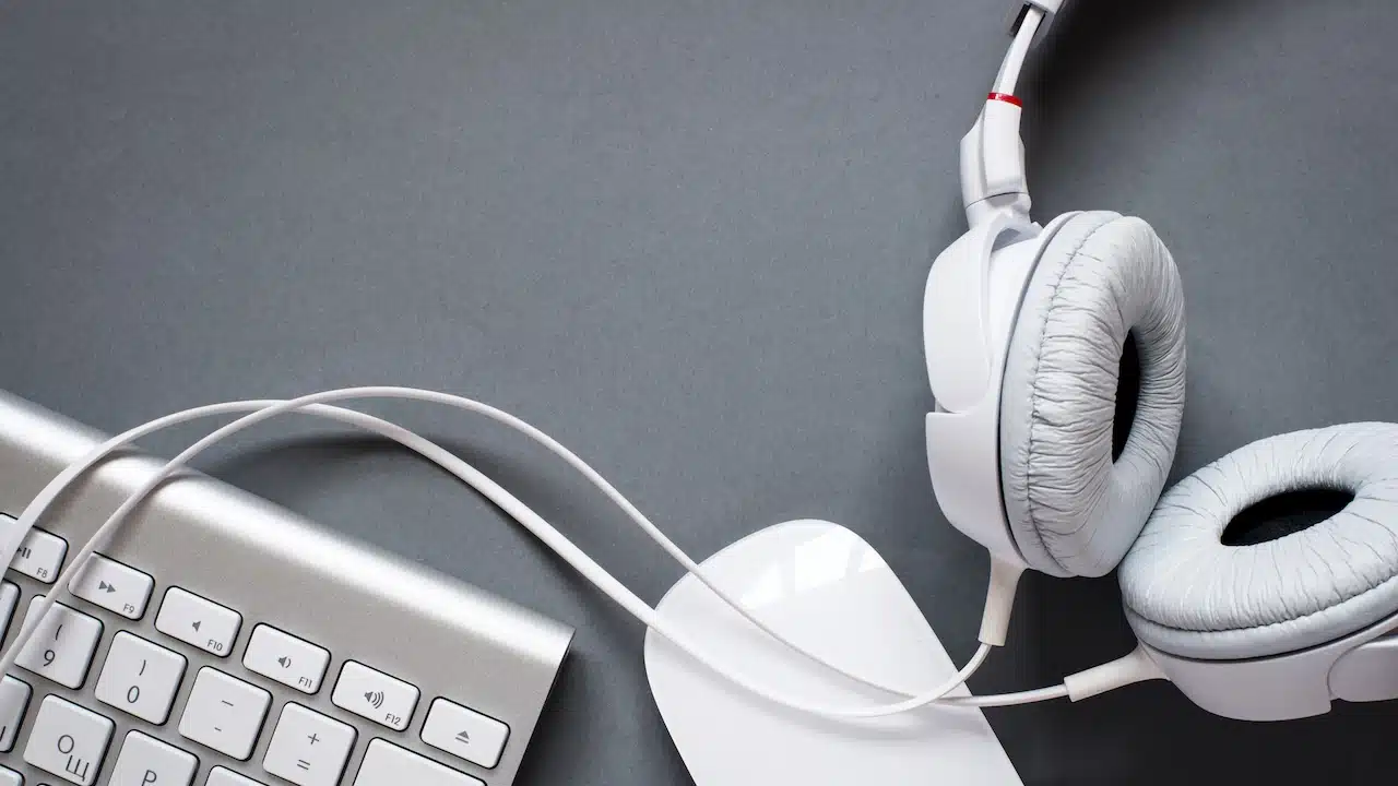 High Angle View of Modern White Audio Headphones with Cord, Mac Computer Keyboard and Mouse on Grey Desk Background