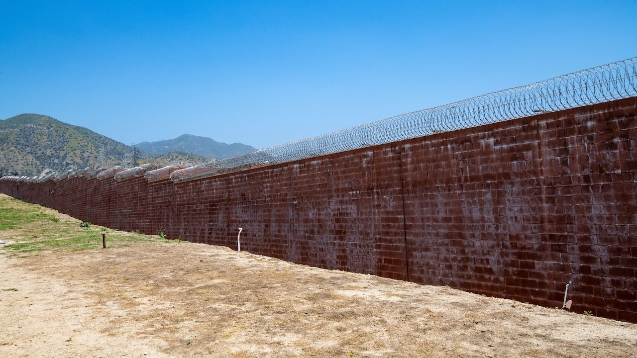 Brick wall with razor wire, correctional facility, prison wall, mountain in background. Barry J. Nidor Juvenile Hall facility, wall, razor wire. Correctional facility, criminal justice.