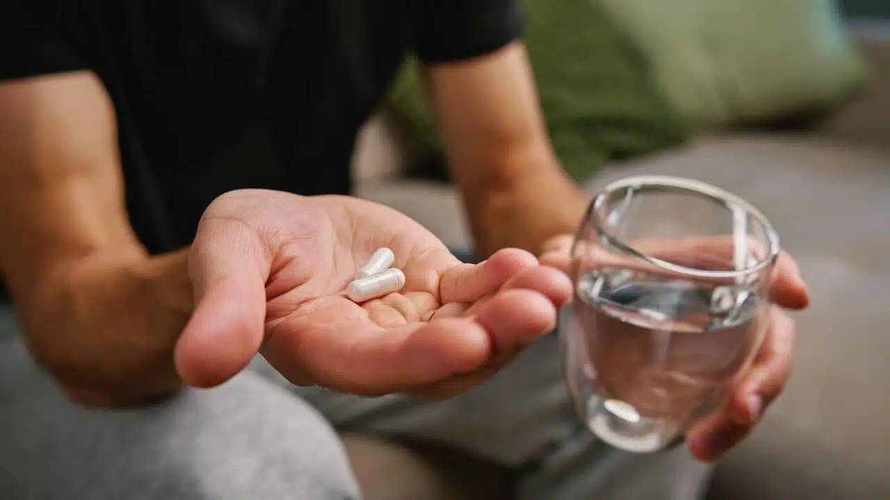 Man holds two pills in one hand and glass of water in other