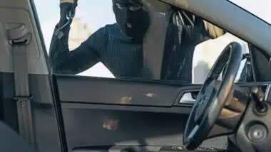 View from the car at the man dressed in black with a balaclava on his head preparing breaking with crowbar the glass of car before the stealing.