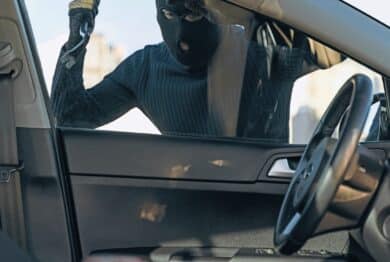 View from the car at the man dressed in black with a balaclava on his head preparing breaking with crowbar the glass of car before the stealing.