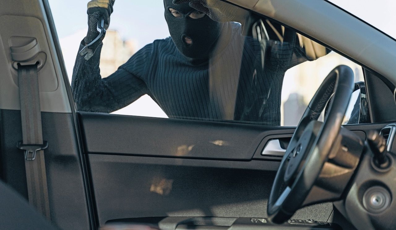 View from the car at the man dressed in black with a balaclava on his head preparing breaking with crowbar the glass of car before the stealing.