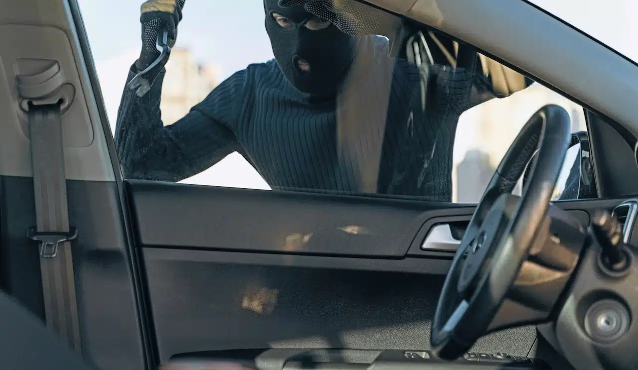 View from the car at the man dressed in black with a balaclava on his head preparing breaking with crowbar the glass of car before the stealing.