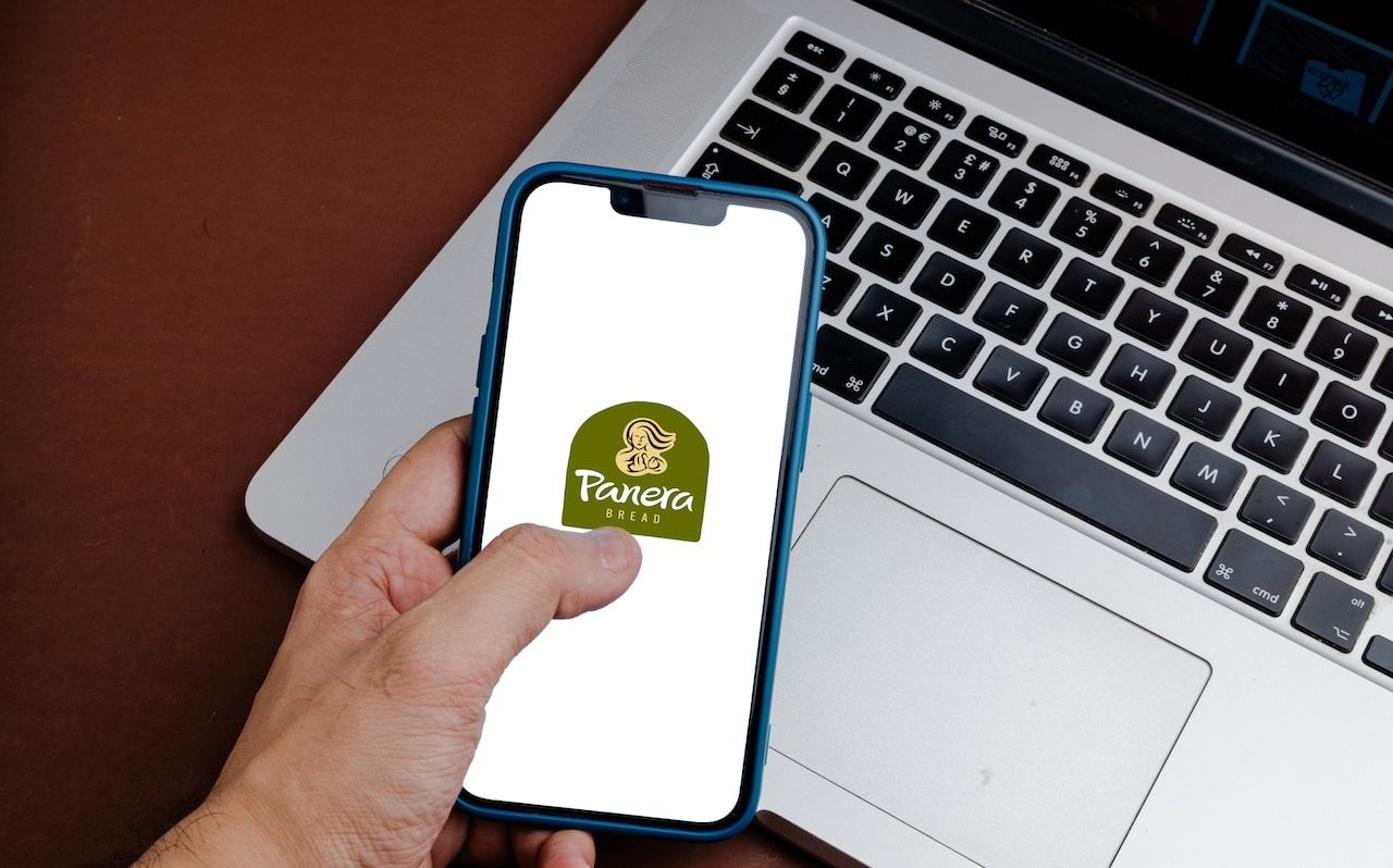 Panera Bread bakery logo on phone in front of laptop.