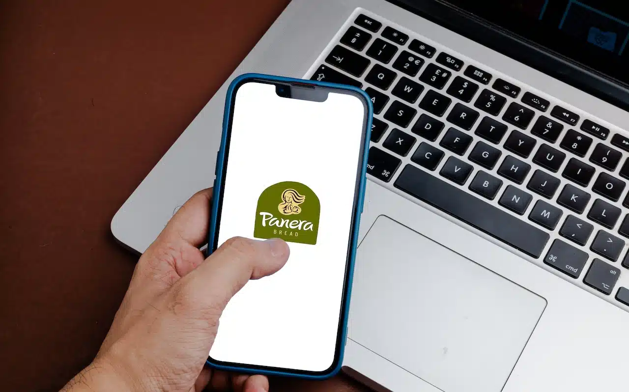 Panera Bread bakery logo on phone in front of laptop.