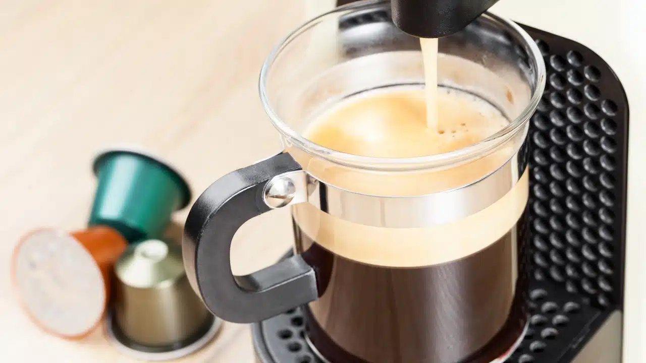 Single-serving coffee machine dispenses espresso in a glass cup with coffee capsules in background
