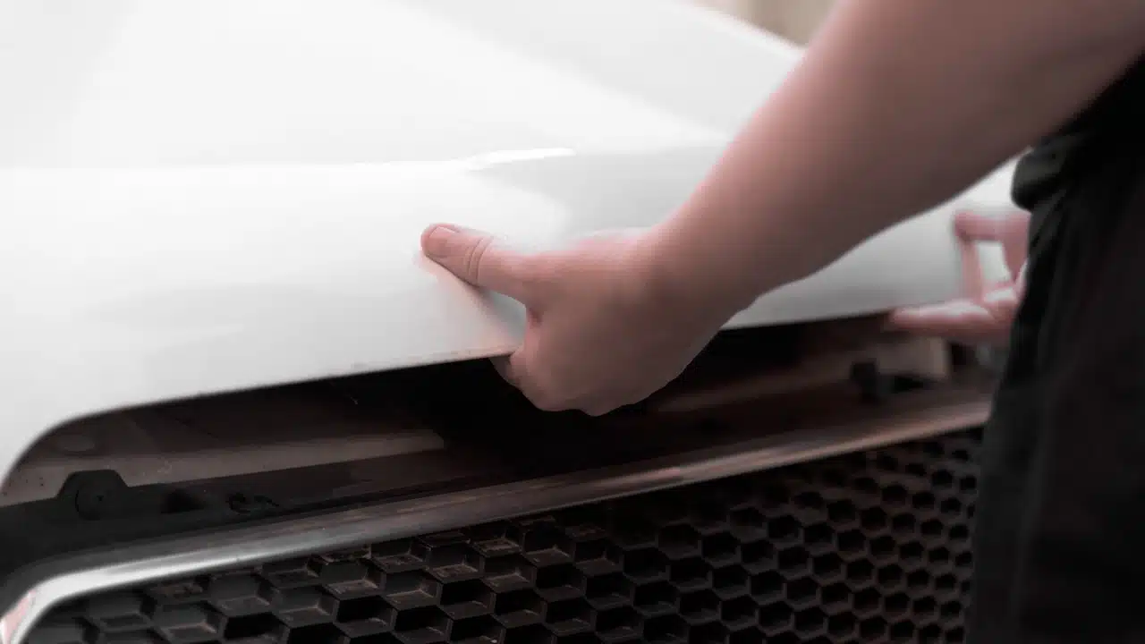 hands in black casual clothes opening the hood of a white car.