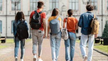 Group of five students with backpacks walking at university campus