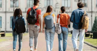 Group of five students with backpacks walking at university campus