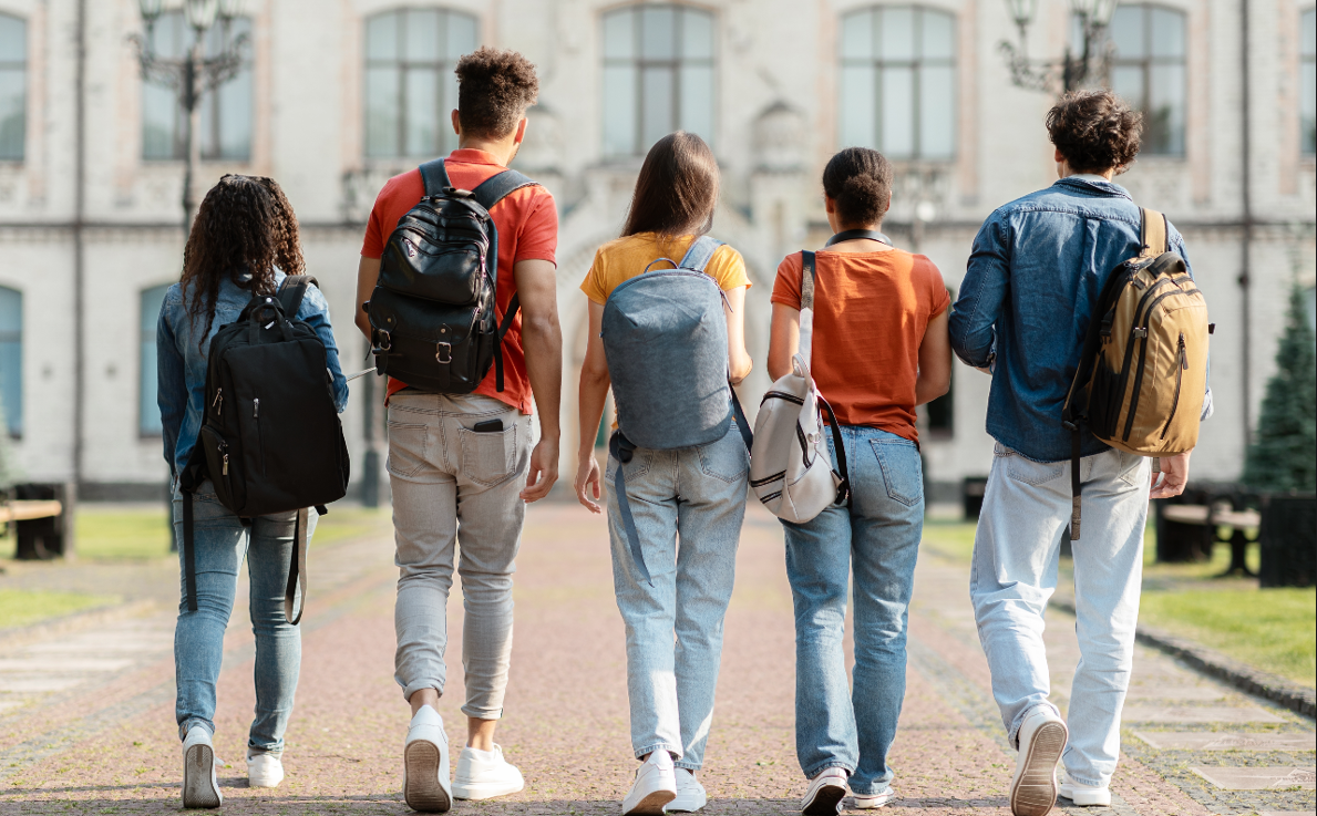 Group of five students with backpacks walking at university campus