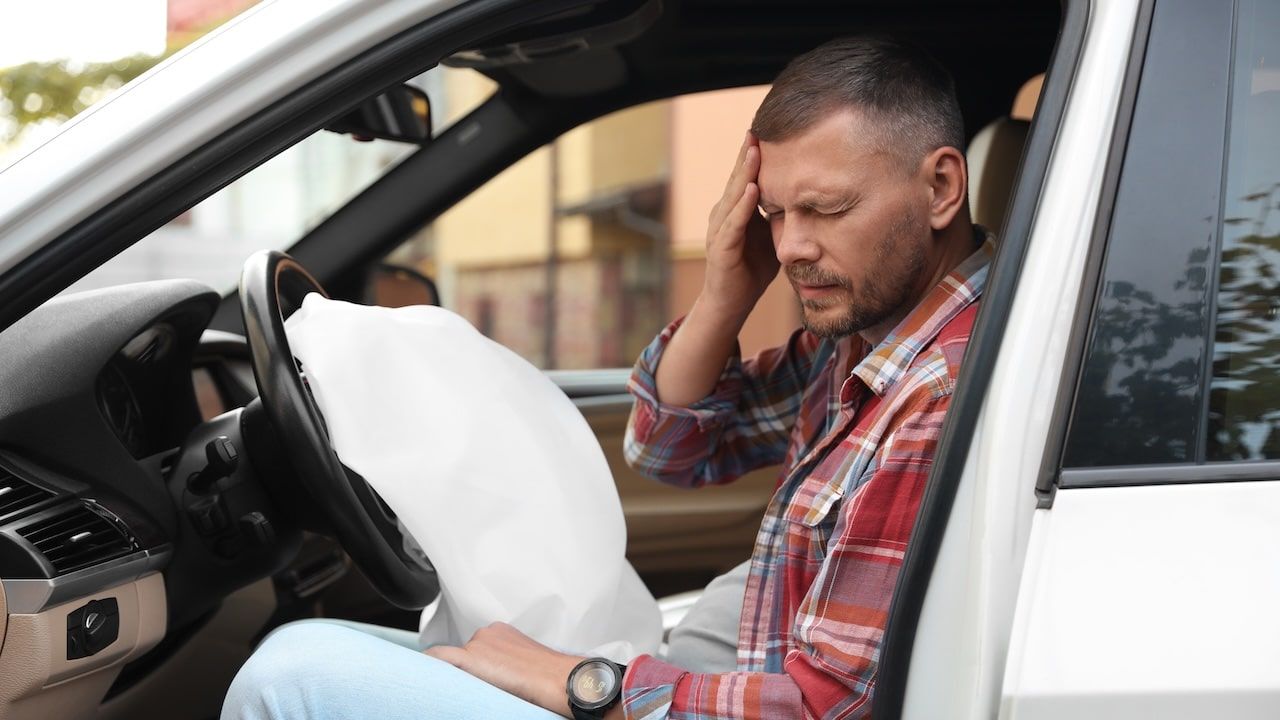Injured man near opened airbag in automobile after car accident