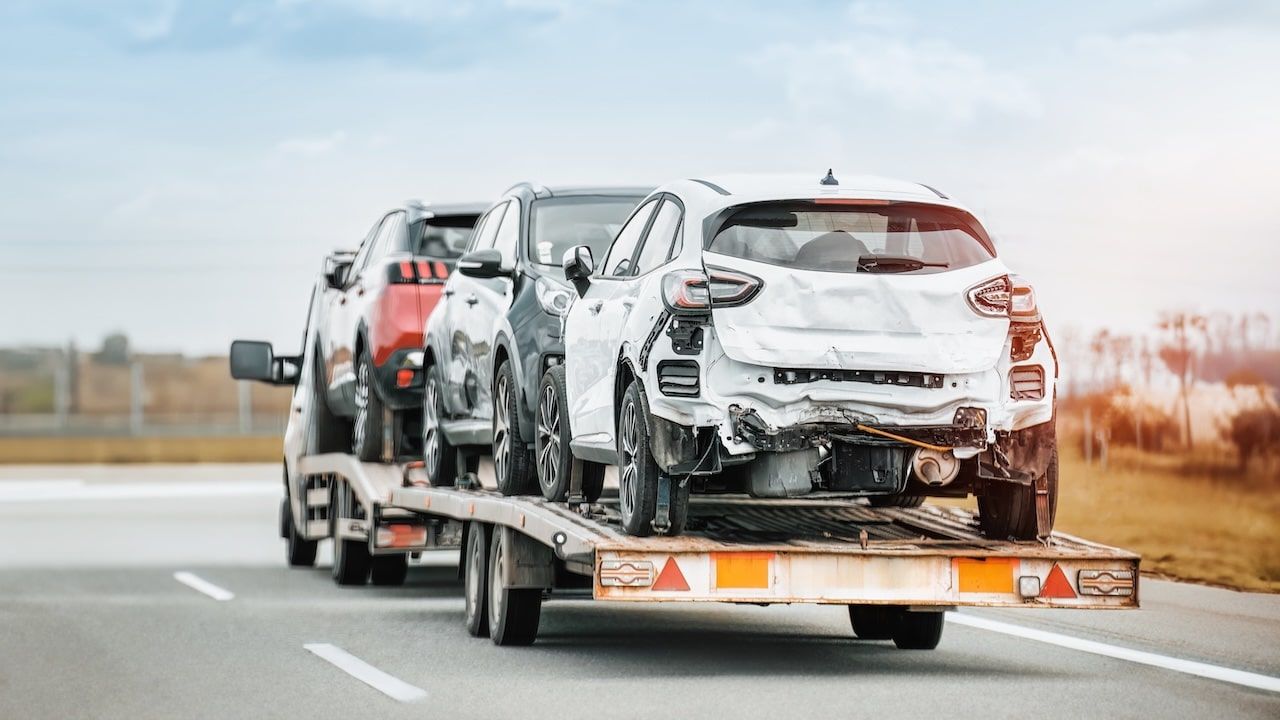 Rear view of tow truck transporting 3 totaled damaged cars.
