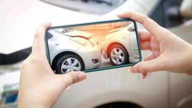 A woman holds a smartphone to take pictures of the area of ​​a car crash in the accident.