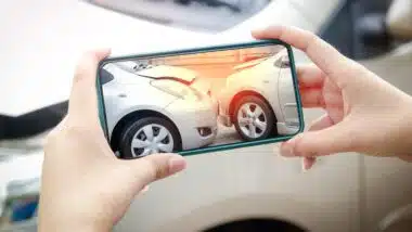 A woman holds a smartphone to take pictures of the area of ​​a car crash in the accident.