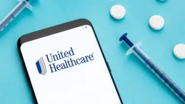 Unitedhealthcare logo on Smart phone screen pills and syringe on blue background