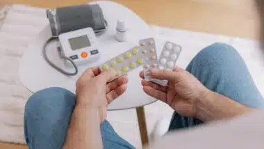 Close-up of elderly man sitting sofa at living room measures blood pressure with device.