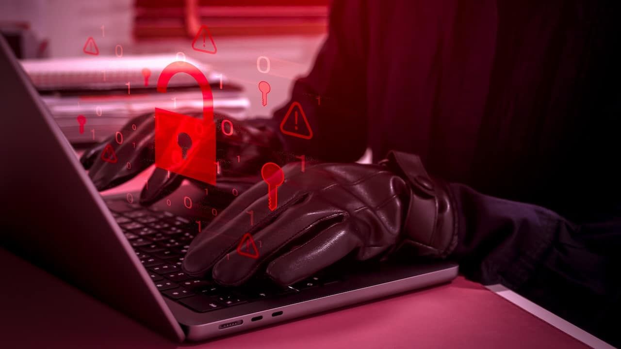 Cybersecurity threat concept showing hacker or scammer using laptop with glowing red unlocked padlock icon