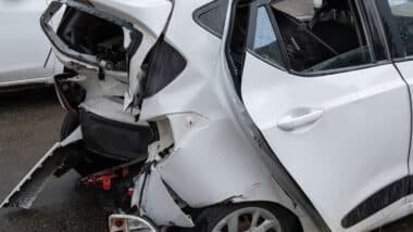 The rear of a white car shows severe collision damage