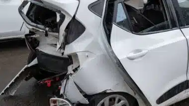The rear of a white car shows severe collision damage