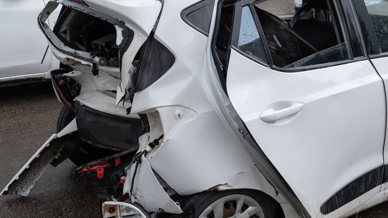 The rear of a white car shows severe collision damage