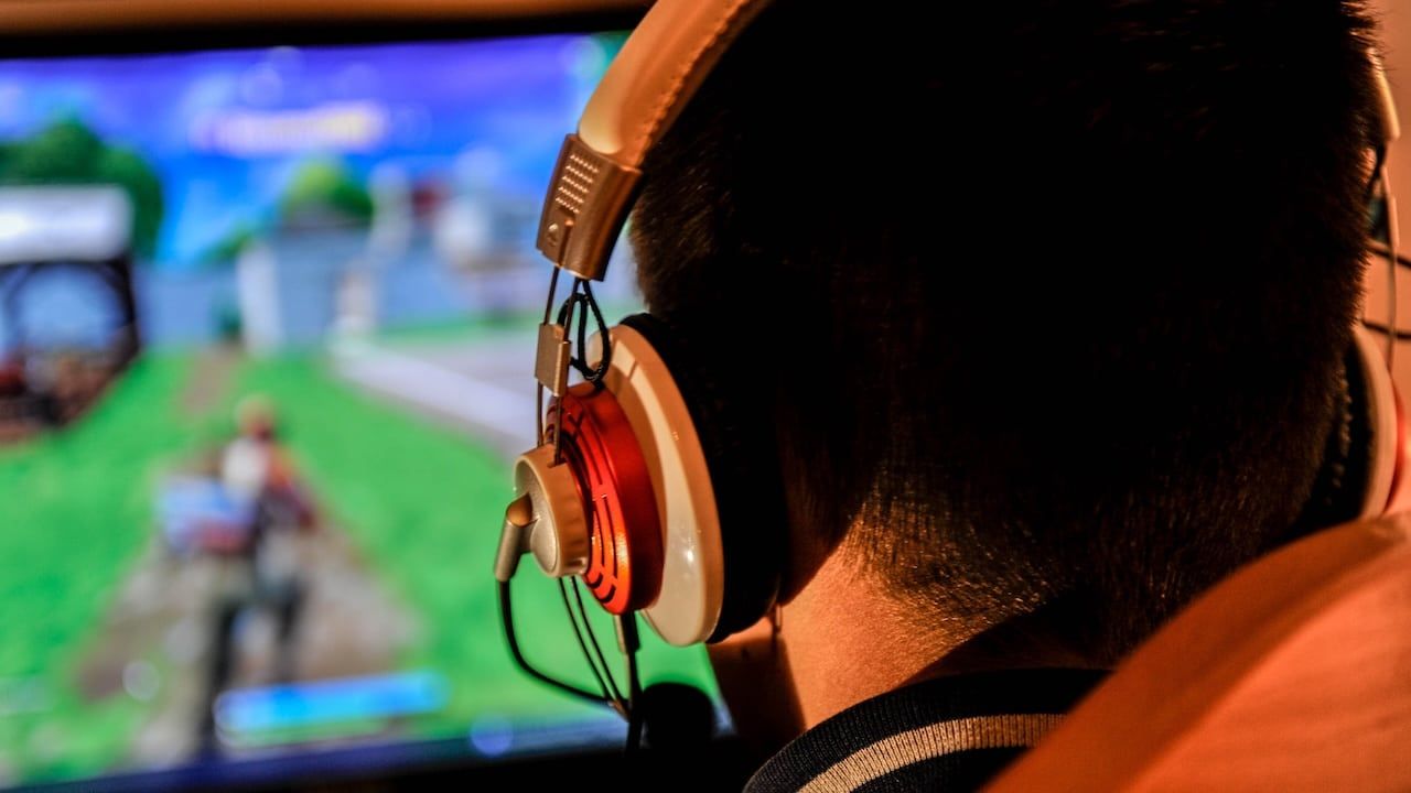 A young gamer boy playing video games on computer wearing headphones and colorful keyboard.