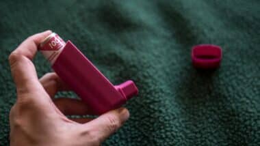 Hand Holding Asthma Inhaler on Dark Background