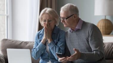 Shocked upset elderly couple getting bad news, finding fraud, money stealing, loss, overspending, financial problem, holding calculator, using laptop, staring at monitor