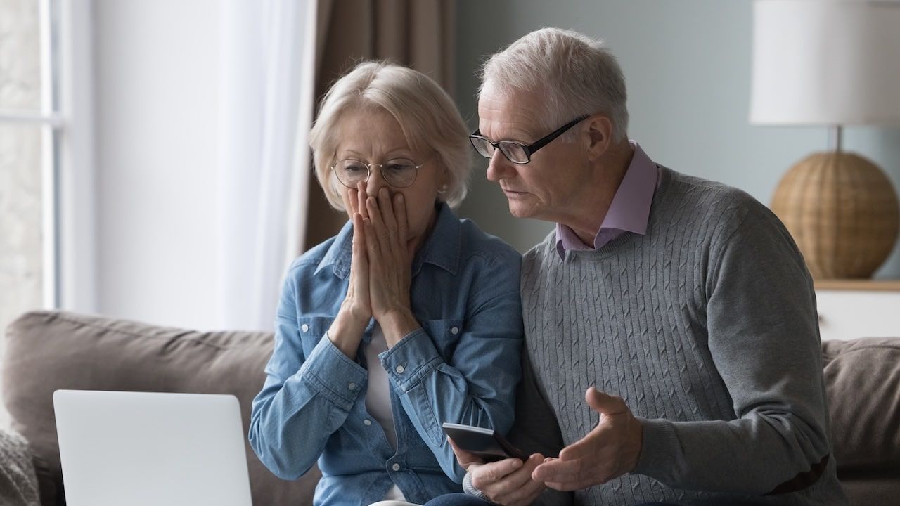 Shocked upset elderly couple getting bad news, finding fraud, money stealing, loss, overspending, financial problem, holding calculator, using laptop, staring at monitor