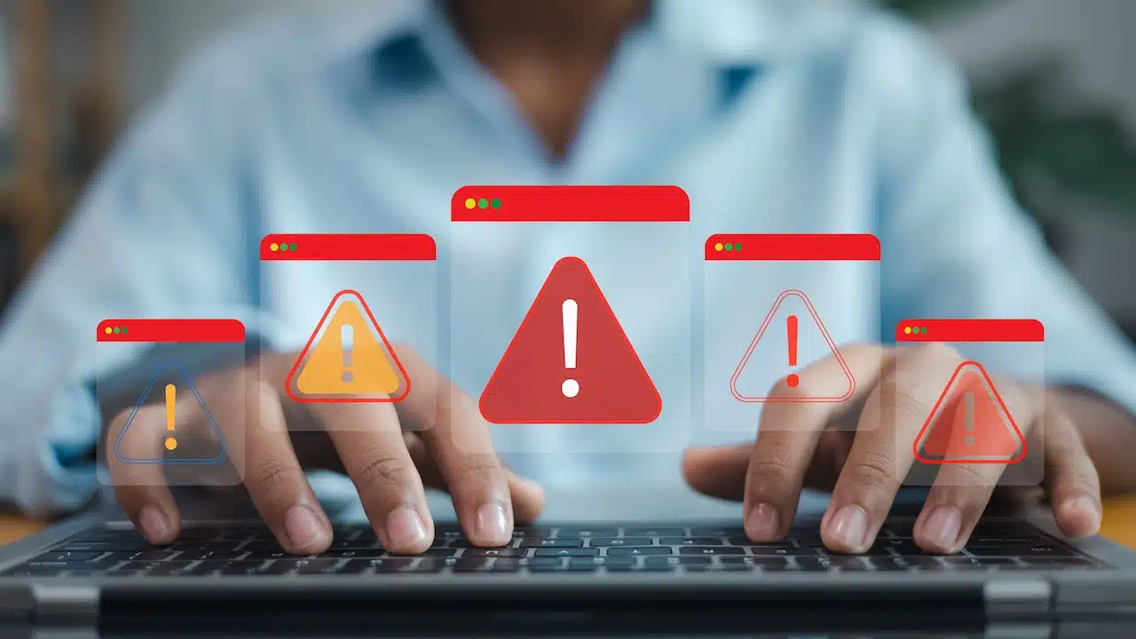 Person typing on laptop with multiple security alert warning windows, symbolizing cyber threat, data breach
