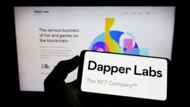 Person holding mobile phone with logo of Canadian blockchain company Dapper Labs Inc. on screen in front of web page.