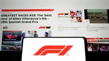 Formula 1 logo displayed on a mobile phone with its website homepage in the background, F1 is the highest class of single-seater car racing.
