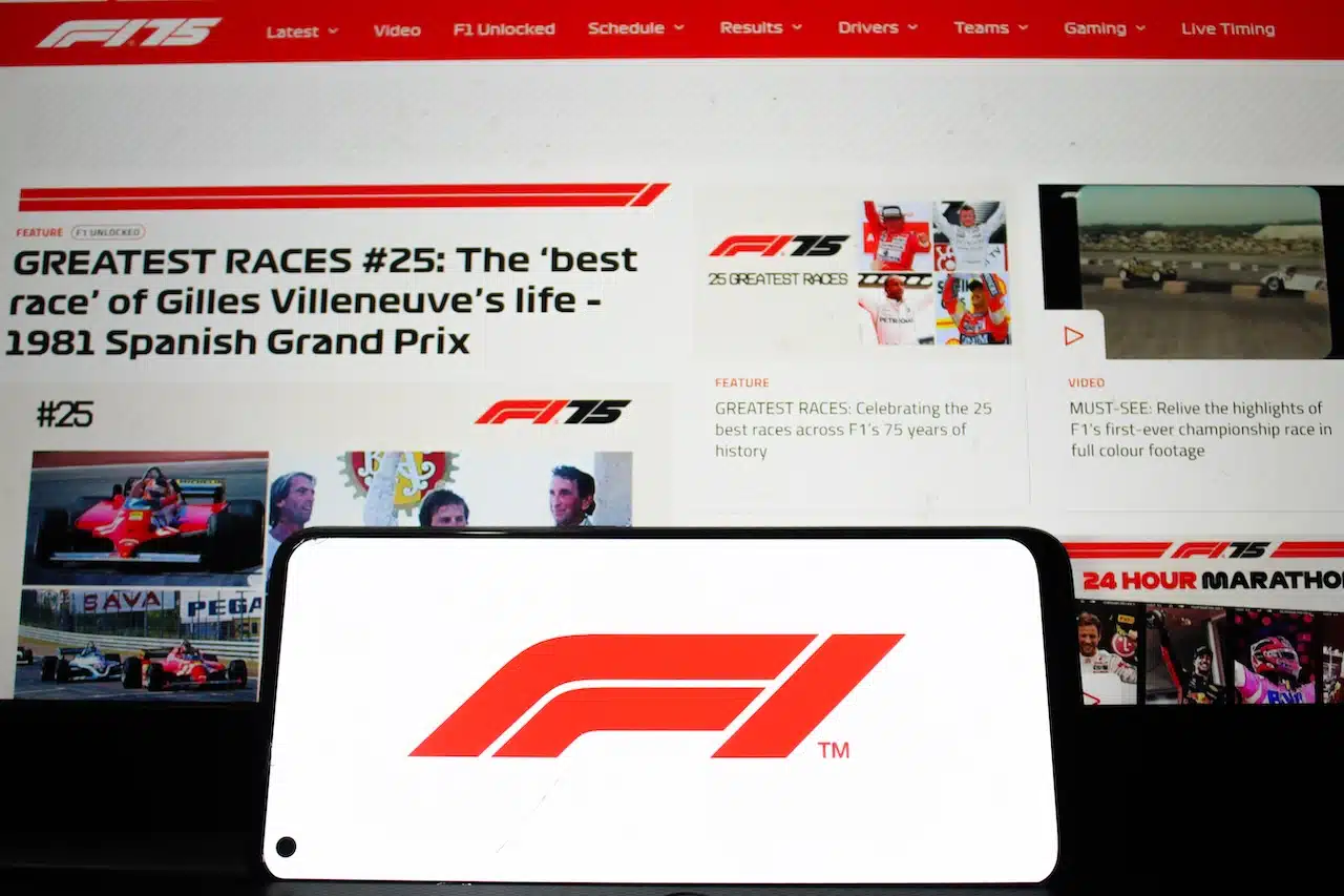 Formula 1 logo displayed on a mobile phone with its website homepage in the background, F1 is the highest class of single-seater car racing.