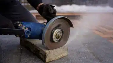 cutting concrete curb with angle grinder, rotating abrasive disc trimming paving stone for sidewalk installation and urban landscaping work.