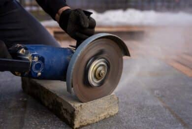 cutting concrete curb with angle grinder, rotating abrasive disc trimming paving stone for sidewalk installation and urban landscaping work.