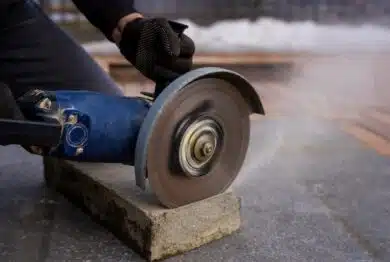 cutting concrete curb with angle grinder, rotating abrasive disc trimming paving stone for sidewalk installation and urban landscaping work.