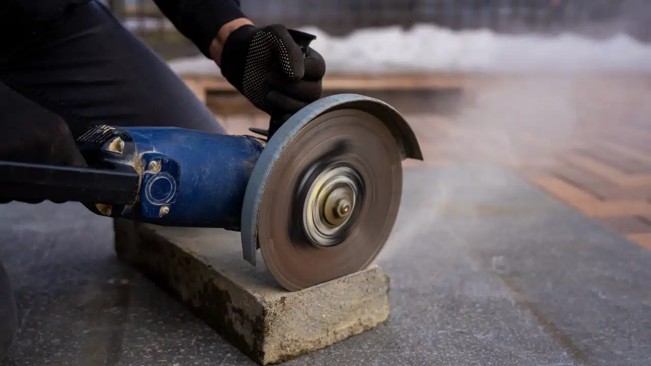cutting concrete curb with angle grinder, rotating abrasive disc trimming paving stone for sidewalk installation and urban landscaping work.