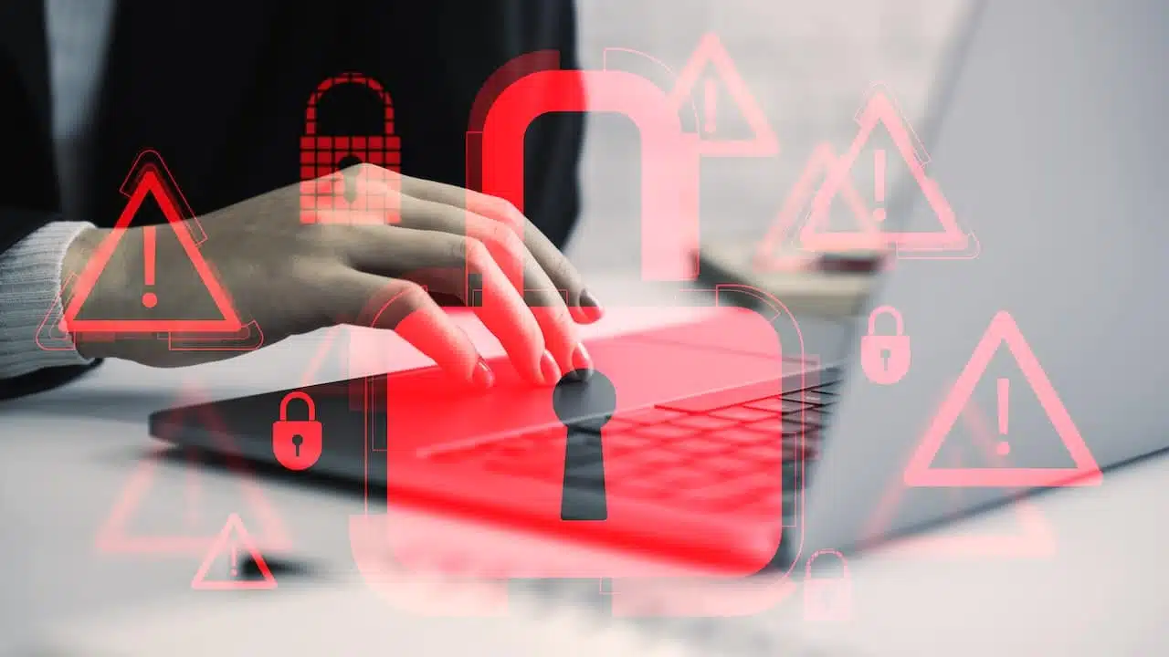 Hands on laptop keyboard with red padlock and alert icons in modern digital style on light background, concept of cyber attack and data security breach