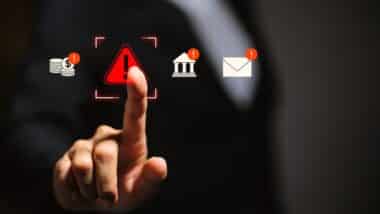Businessman touching glowing red warning triangle icon surrounded by financial, banking, and email alert notifications, representing cyber fraud risk, financial threat, and security breach concept.