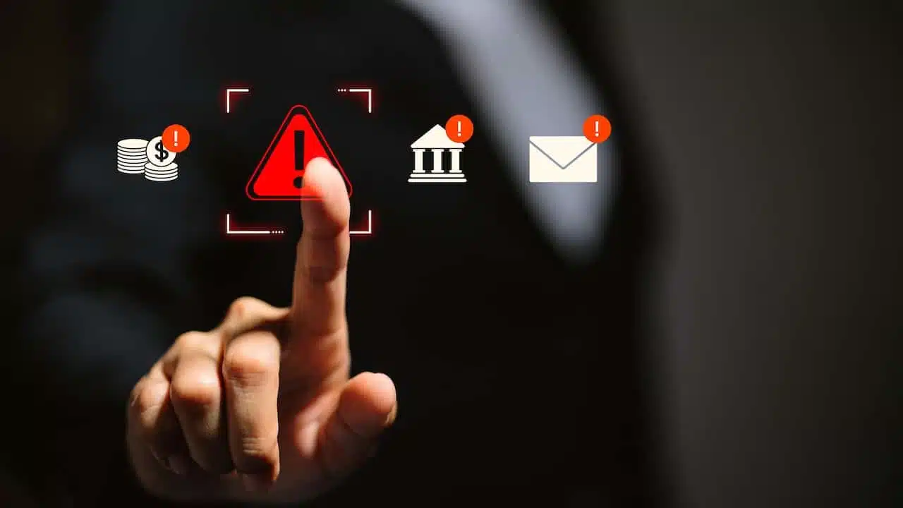 Businessman touching glowing red warning triangle icon surrounded by financial, banking, and email alert notifications, representing cyber fraud risk, financial threat, and security breach concept.